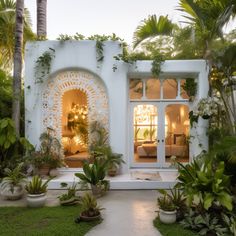 a white house with lots of plants and trees in front of the entrance to it