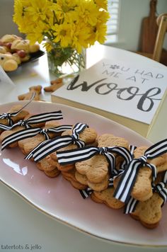 cookies tied with black and white ribbons are on a pink plate next to a bouquet of yellow flowers