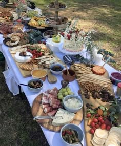 a table full of food sitting on top of a grass covered field next to trees