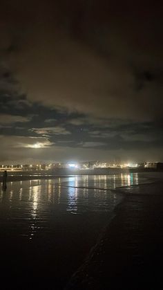 the beach is lit up at night and people are walking on the sand near the water