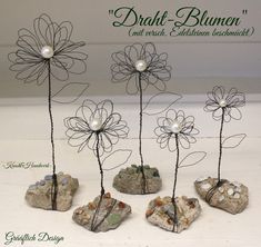 four metal flowers with pearls on them sitting next to rocks and stones in the shape of hearts