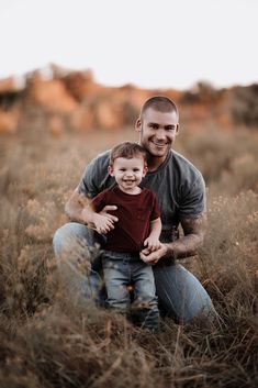 a man holding a small boy in his arms while sitting on top of a field