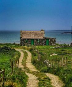 an old stone house sitting on top of a lush green field next to the ocean