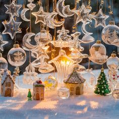 an assortment of glass ornaments hanging from strings in the snow with houses and trees around them