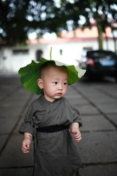 a young child with a green leaf on top of it's head walking down the street