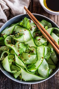 a bowl filled with sliced cucumber and chopsticks next to some dipping sauce