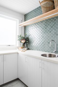 a kitchen with white cabinets and green tiles on the backsplash, along with a stainless steel sink