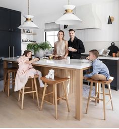 a group of people standing around a kitchen island with two children sitting on the counter