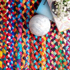 a multicolored rug next to a vase with flowers and a book on it