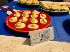 some deviled eggs are on a red plate and blue tablecloth with other dishes in the background