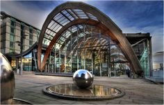 a large metal ball sitting on top of a fountain in front of a glass building