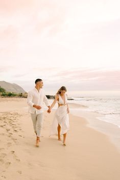 a man and woman walking on the beach holding hands