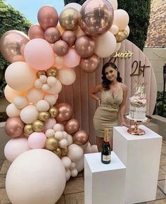 a woman standing in front of a cake and balloons display at a birthday party with champagne