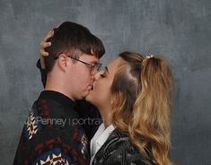 a man and woman kissing each other in front of a gray wall with black background