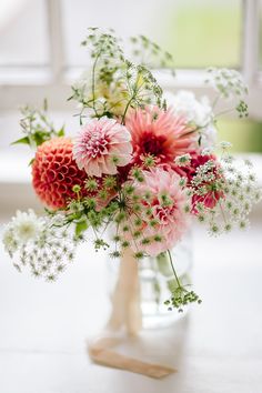 a vase filled with pink and white flowers on top of a table next to a window