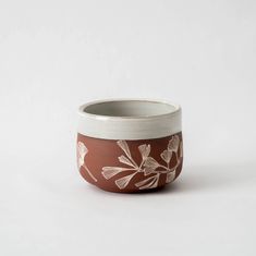 a brown and white bowl with flowers painted on the side, sitting against a white background