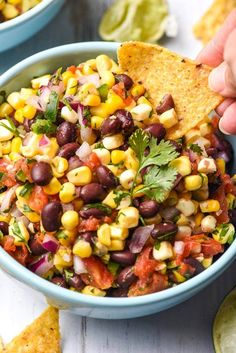 a hand dipping a tortilla chip into a bowl filled with corn and black beans