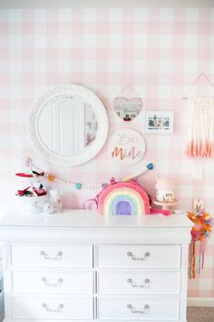 a white dresser sitting next to a pink and white checkered wall with a mirror above it