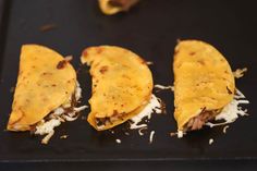 three tortillas on a black tray with shredded cheese and other toppings next to an orange