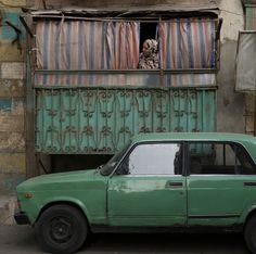 an old green car parked in front of a building with a skeleton on it's head