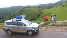 a car parked on the side of a road with people standing around it and hills in the background