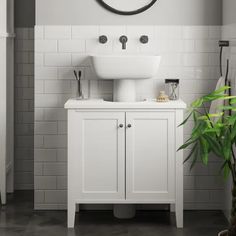 a white sink sitting under a mirror next to a green plant