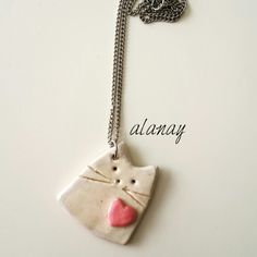 a white ceramic cat with a pink heart on it's face hanging from a silver chain