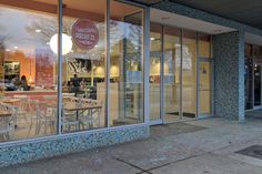 the outside of a restaurant with tables and chairs in front of glass doors that are open