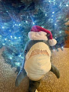 a stuffed shark with a santa hat on it's head sitting in front of a christmas tree