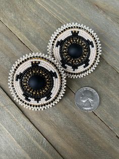 two black and white beaded earrings sitting on top of a wooden table next to a dime