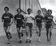 a group of young men and women running down a street in front of a building