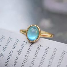 This ring features a striking oval blue gemstone with a smooth, polished cabochon cut, which enhances the stone's vibrant color and depth. The gemstone is set in a simple gold bezel setting that wraps around its edges, creating a clean and modern look. The band is made of gold and is slender, complementing the elegance of the gemstone without overwhelming it. The overall design is minimalistic and sophisticated, highlighting the beauty of the blue stone. Details Isabella Oval Blue Gemstone Vintage Ring Adjustable opening Gold band Rare, antique design Reyis Jewelry Isabella Collection Vintage Gemstone Rings, Gemstone Rings Vintage, Pearl Jewelry Necklace, Natural Stones Necklace, Gold Statement Earrings, Natural Stone Jewelry, Natural Stone Bracelets, Antique Design, Anklet Jewelry