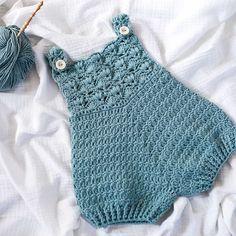 a blue crocheted baby romper laying on top of a bed next to a ball of yarn