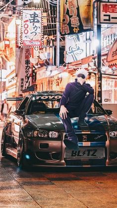 a man sitting on top of a car in the middle of a city at night