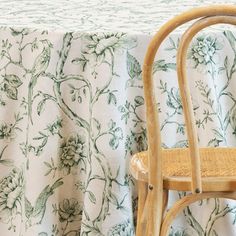 a wooden chair sitting next to a table covered in a white and green floral print