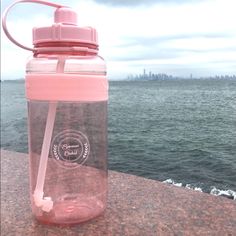 a water bottle with a straw sticking out of it sitting on a ledge near the ocean