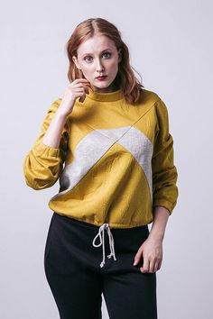 a woman in a yellow sweater poses for the camera with her hand on her chin