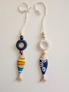 two wooden beads are hanging from strings on a white surface, one is shaped like a fish and the other has a beaded ring