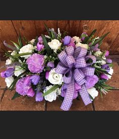 a purple and white flower arrangement in front of a wooden door with a bow on it