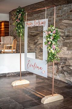 a sign that says happy birthday next to some flowers and greenery on the side of a stone wall