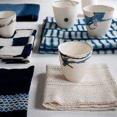 a table topped with blue and white placemats next to cups on top of napkins