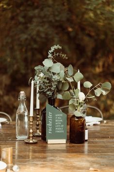 a wooden table topped with bottles filled with flowers and greenery on top of it