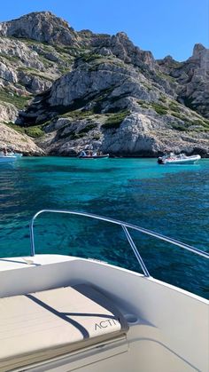 the boat is traveling through the clear blue water near rocky mountains and cliffs in the distance