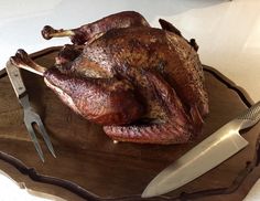 a roasted turkey on a wooden platter with knifes and a paring knife