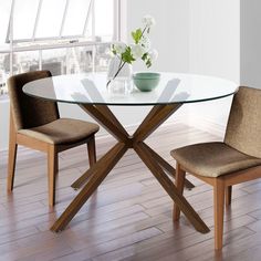 a glass dining table with two chairs and a vase on the top, in front of a window