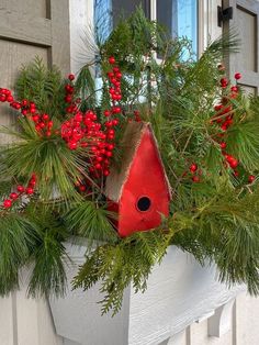 a red birdhouse sitting on top of a window sill filled with greenery