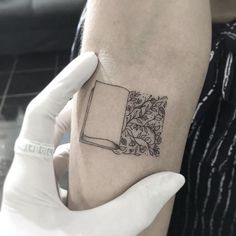 a book tattoo on the left inner arm and wrist is shown in black ink, with leaves surrounding it