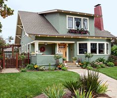 a green house with white trim and flowers in the front yard, on a sunny day