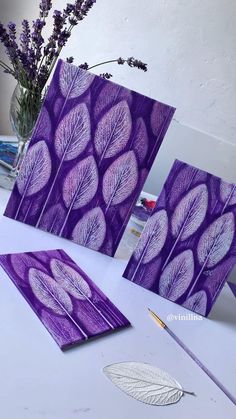 three cards with purple leaves on them sitting on a table next to a vase filled with flowers