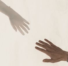 two hands reaching out towards each other in front of a white wall with the shadow of someone's hand on it